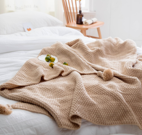 Knitted throw with pom-pom fringe on a sofa