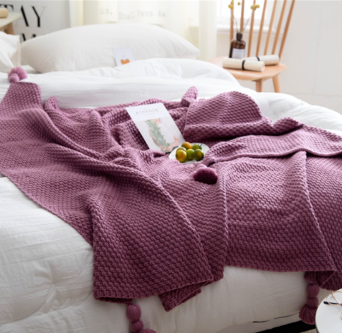 Knitted throw with pom-pom fringe on a sofa