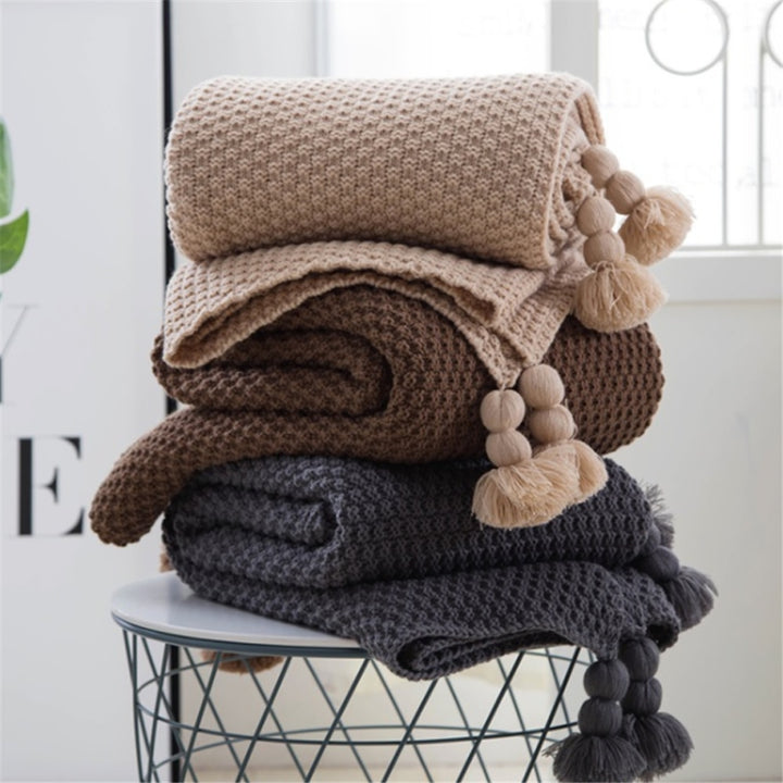 Knitted throw with pom-pom fringe on a sofa